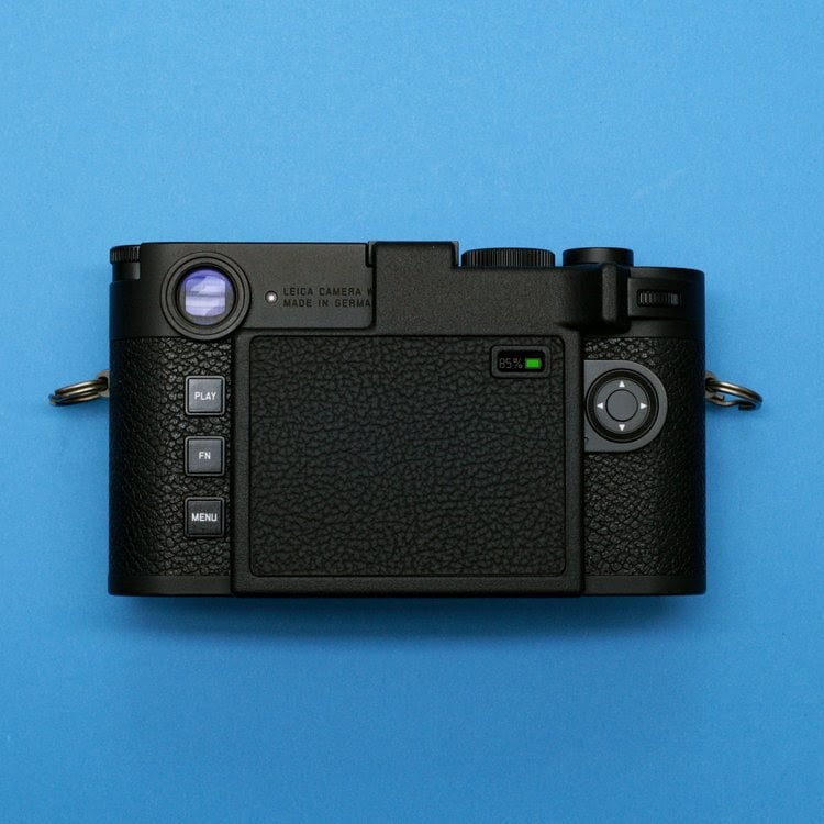 A black digital camera shown from the back, featuring textured grip, control buttons, and a small screen, all set against a solid blue background.
