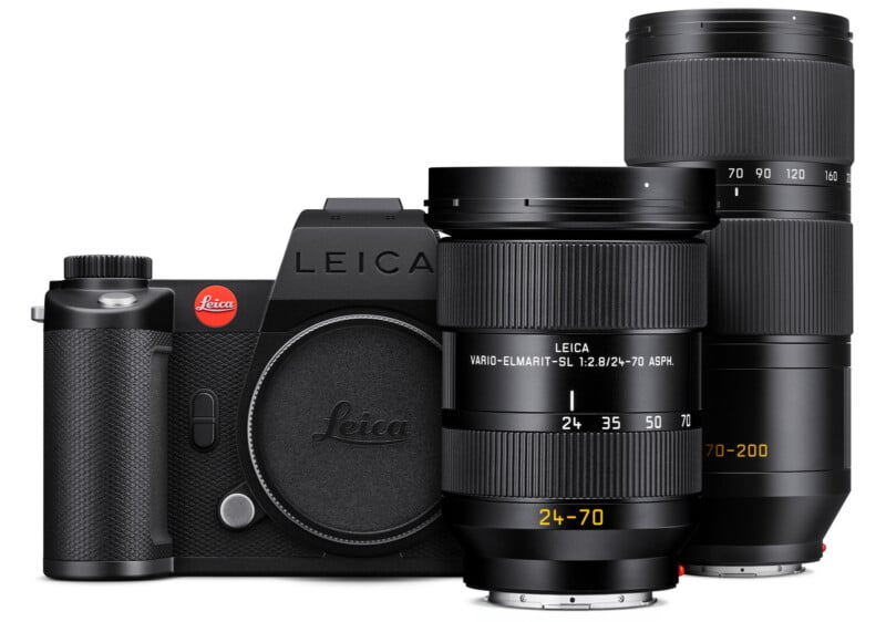 A black Leica camera with two interchangeable lenses, a 24-70mm lens attached to the camera and a 70-200mm lens standing upright beside it against a white background.