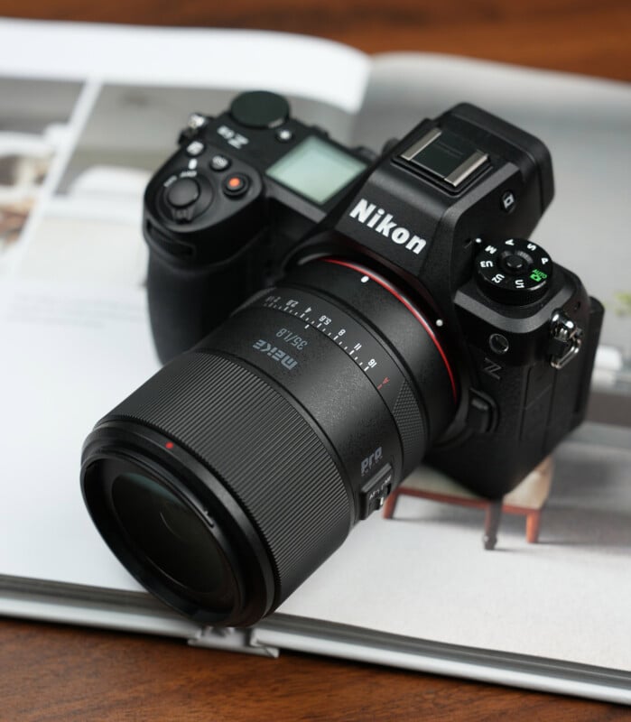 A Nikon digital camera with a large lens is resting on an open magazine, placed on a wooden surface.
