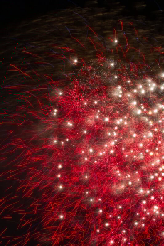 Bright red and white fireworks burst against a dark night sky, creating vibrant streaks and sparkling patterns that fill the right side of the image.