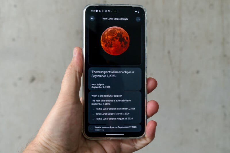 A hand holds a smartphone displaying information about a lunar eclipse, featuring an image of a red moon and text stating the next partial lunar eclipse is on September 7, 2025.