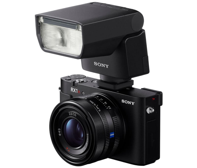 A black Sony RX1 digital camera with a large detachable flash mounted on top, shown on a white background.