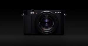 A black Sony RX1R II digital camera with a prominent Zeiss lens, shown from the front against a solid black background.