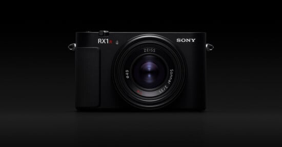 A black Sony RX1R II digital camera with a prominent Zeiss lens, shown from the front against a solid black background.