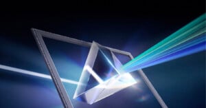 A beam of light passes through a transparent glass prism, splitting into multiple colored rays, against a dark background. The scene suggests the dispersion of light into its spectrum.