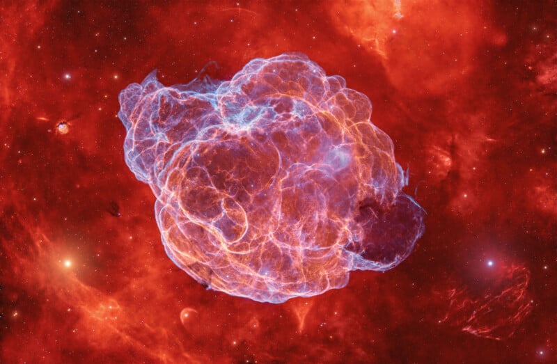 A glowing, cloud-like nebula with blue and orange hues floats against a vibrant red cosmic background filled with scattered stars.