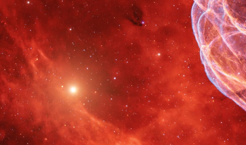 A bright star glows amid a red-hued nebula scattered with small stars. On the right edge, wispy blue and white filaments curve against the vibrant cosmic background.