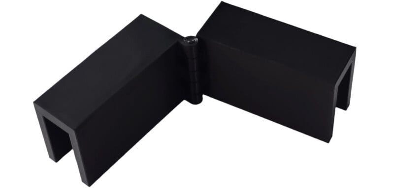 A black, V-shaped metal hinge bracket with two rectangular arms connected at the center by a cylindrical hinge, displayed on a white background.