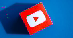 A cube with the YouTube play button logo on a red face, placed on a blue background with a shadow cast to the left.