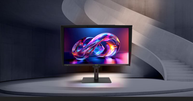 A computer monitor displaying a vibrant, abstract infinity symbol stands on a modern circular platform, with a curved concrete staircase and walls in the background.
