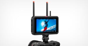 A digital camera with a mounted Atomos Ninja video monitor displaying a snowboarder mid-air against a bright blue sky, with two antennas extending from the monitor for wireless connectivity.