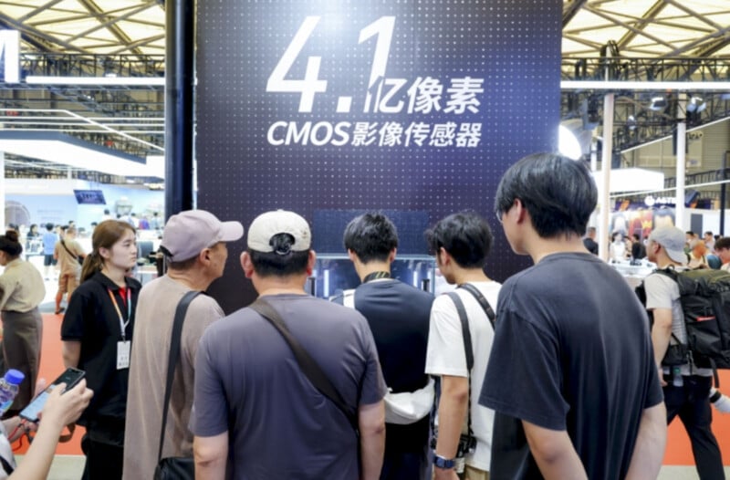 A group of people stands in front of a large display at a tech exhibition. The display features bold text in Chinese and English, highlighting a 410 million pixel CMOS image sensor. The background shows a busy expo setting.