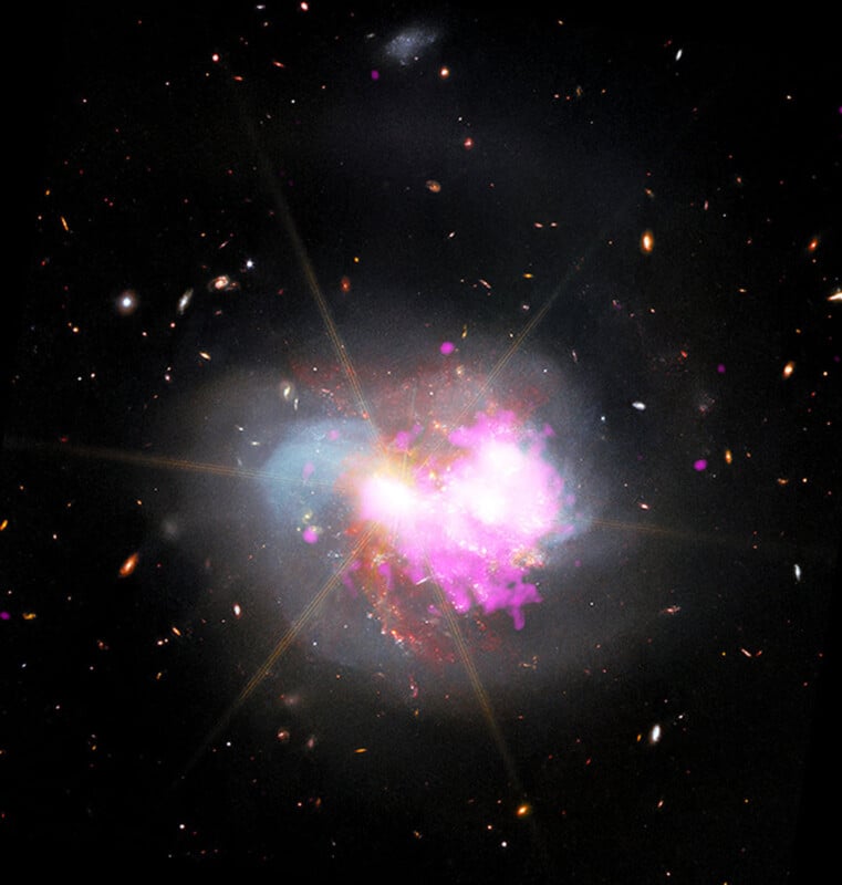 A vibrant, colorful galaxy collision with bright flashes of pink, purple, and yellow light at the center, surrounded by scattered stars and faint galaxies against a dark background.