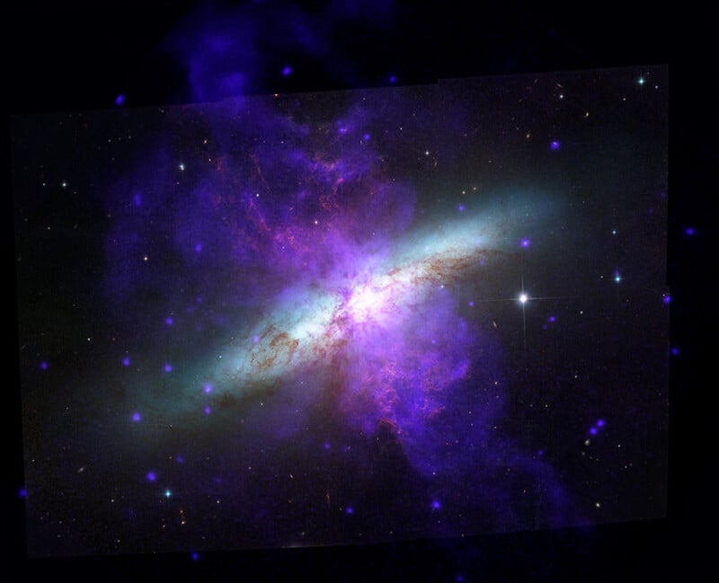 A colorful image of a galaxy shows bright purple, blue, and green clouds of gas and dust surrounded by stars, set against the dark backdrop of outer space.