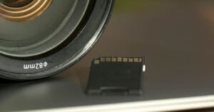 Close-up of a camera lens labeled "82mm" next to a black SD memory card resting on a flat, reflective surface.
