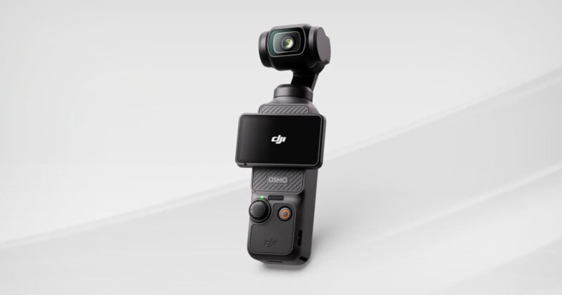 A compact black handheld camera with a built-in gimbal and a flip-out screen displaying the DJI logo, set against a light gray background.