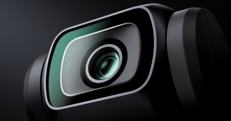 Close-up of a modern digital camera lens with a sleek black and silver design, showing detailed glass elements and smooth curves, set against a dark background.