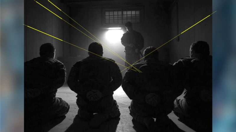 Four people kneel on the floor with their hands behind their backs, facing a standing figure silhouetted in bright light at the end of a dark room. Yellow lines are drawn from the kneeling figures toward the standing figure.