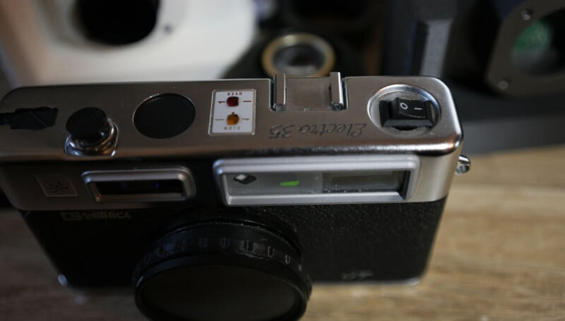 A close-up of the top of a vintage Yashica camera showing the viewfinder, control buttons, and an engraved serial number on a wooden surface.