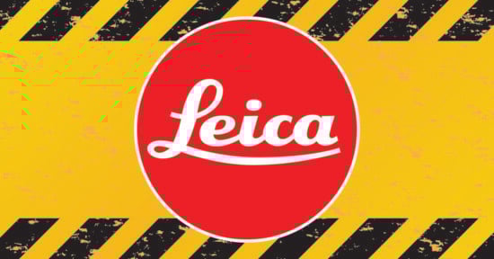 A red oval with the white Leica logo in the center, set against a yellow background with black diagonal hazard stripes along the top and bottom edges.