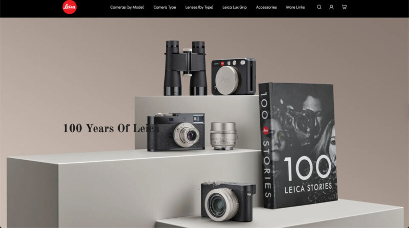 A display of Leica cameras, lenses, binoculars, and a book titled "100 Leica Stories" on geometric platforms, with the text "100 Years Of Leica" on a neutral background.