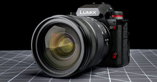 A close-up of a Panasonic Lumix S1 II digital camera with a large lens, placed on a grid-patterned surface against a black background.