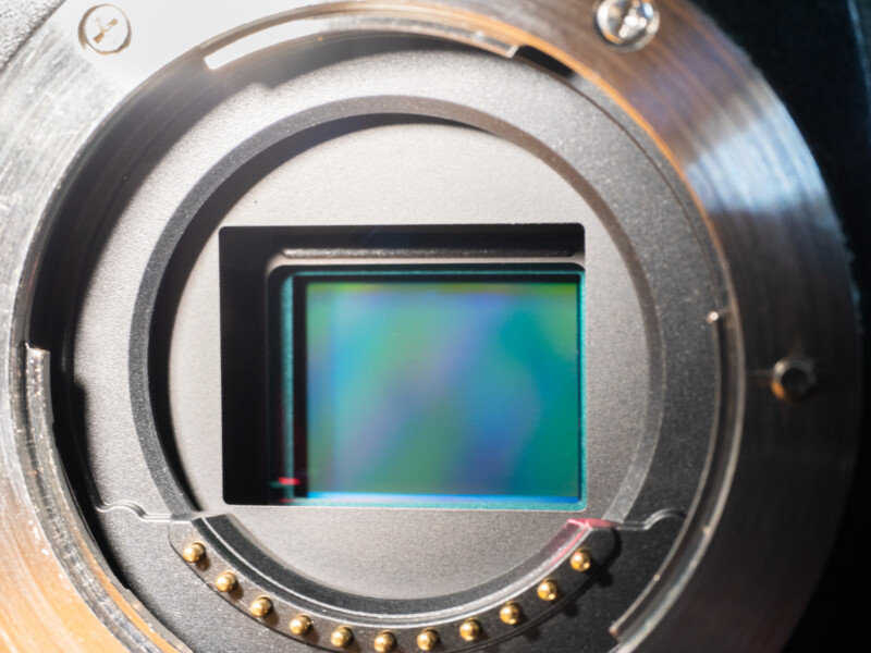 Close-up view of a digital camera sensor inside the camera body, with visible lens mount and electronic contacts surrounding the rectangular sensor.