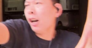A person in a black shirt with an earpiece appears to be in motion, with a blurred, surprised expression, and their arm extended toward the camera. The background shows an indoor setting with metal surfaces.