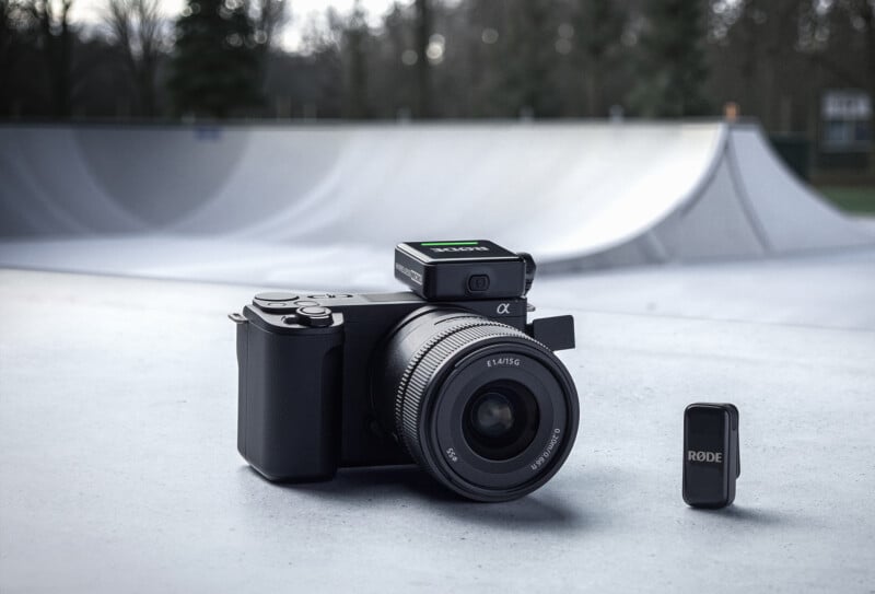 A Sony camera with a lens sits on a concrete surface at a skatepark, with a Rode wireless microphone system placed beside it and a skate ramp visible in the background.