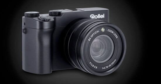 A black Rollei digital camera with an 8x optical zoom lens is shown against a dark gradient background. The lens details and camera controls are clearly visible.