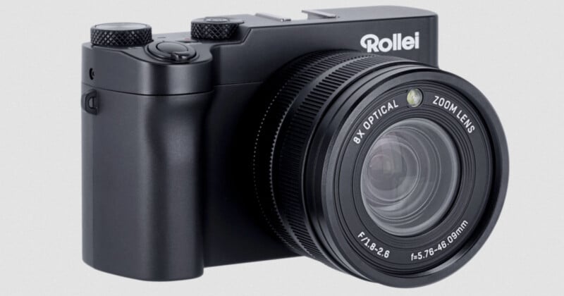 A black Rollei digital camera with a large 8x optical zoom lens, shown angled to highlight the lens and part of the body.