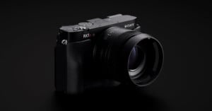 A black Sony RX1R II digital camera with a large lens is shown angled slightly to the right against a dark background.