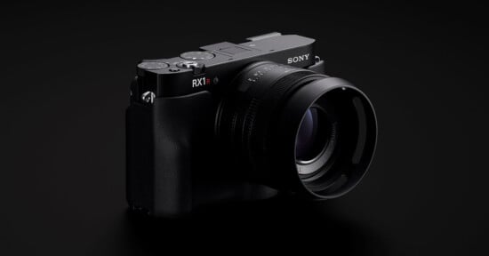 A black Sony RX1R II digital camera with a large lens is shown angled slightly to the right against a dark background.