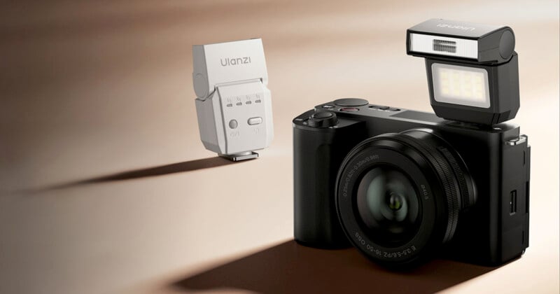 A black digital camera with a lens and an attached external flash faces a white Ulanzi-branded accessory on a beige surface, both well-lit and casting soft shadows.