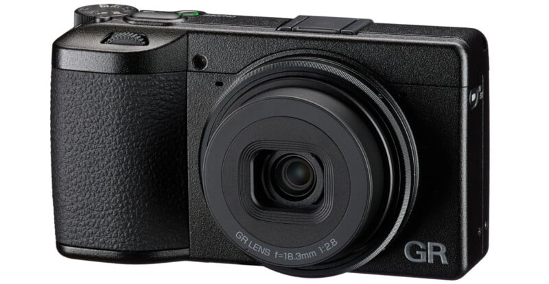A compact black digital camera with a textured grip, lens in the center, and "GR" branding in the lower right corner of the front body.