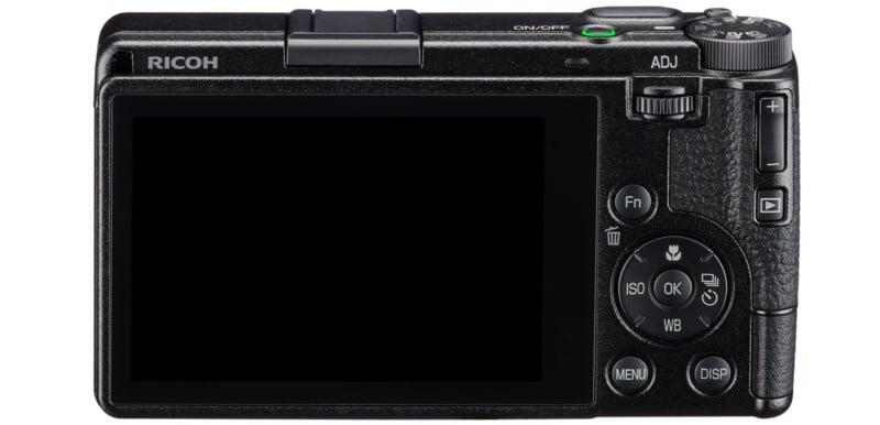 Rear view of a Ricoh digital camera showing a large LCD screen, control buttons, and dials for settings like ISO, menu, and navigation. The camera is black with a textured grip on the right side.
