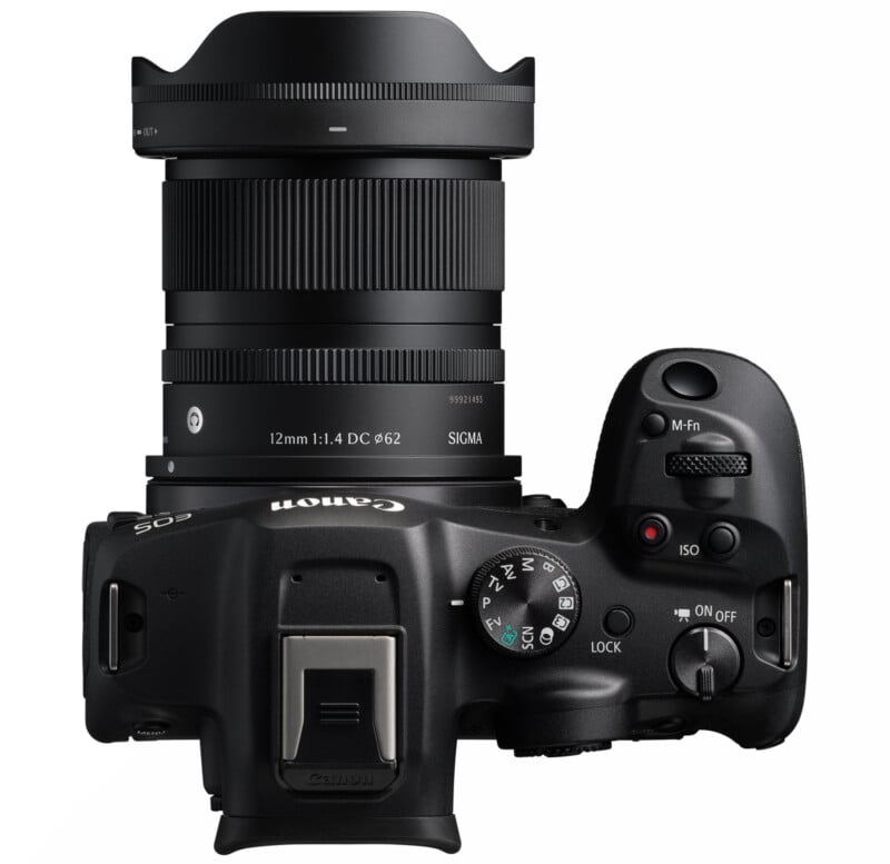 Top view of a black Canon EOS camera with a Sigma 12mm 1:1.4 DC lens attached, showing camera controls, dials, buttons, and part of the lens with clear branding visible.