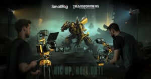 Two filmmakers use camera rigs and equipment to film Bumblebee, a yellow Transformer robot, in a dark, post-apocalyptic city setting. Logos for SmallRig and Transformers are at the top, with "RIG UP, ROLL OUT!" at the bottom.