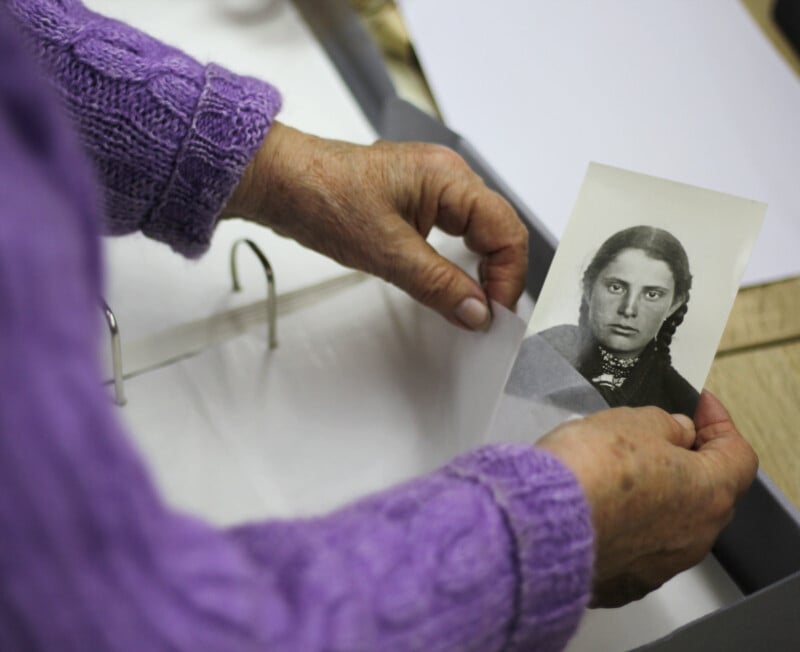 A person wearing a purple sweater is holding a black-and-white portrait of a woman with braided hair, carefully placing it into a binder with plastic sleeves.