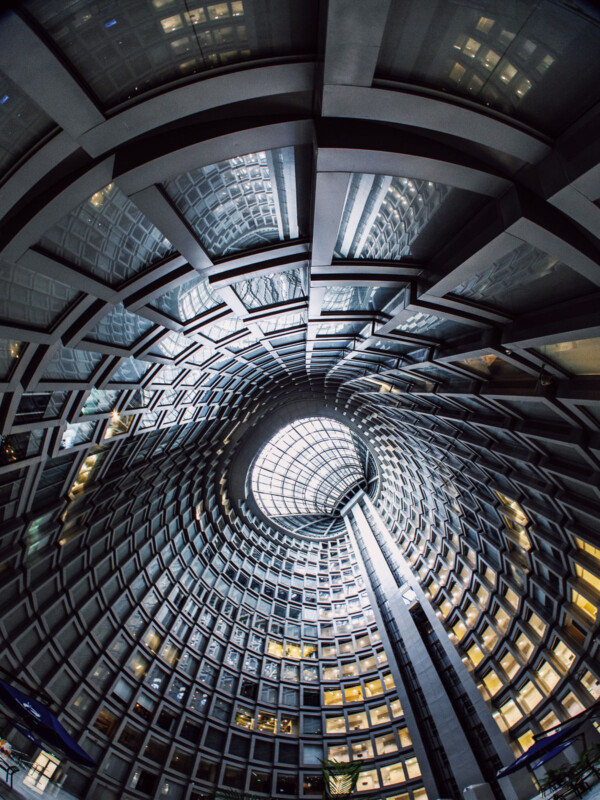 Vista de gran angular mira una gran atrio circular con anillos concéntricos con ventanas, edificios geométricos modernos y techos de vidrio, luz natural desde arriba.
