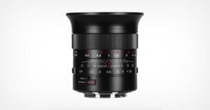 A black camera lens with manual focus and aperture rings, featuring engraved distance and aperture markings in white and red, set against a plain white background.