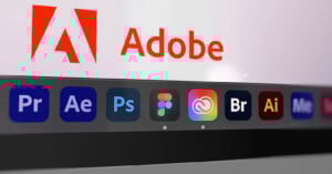 Close-up of a computer screen showing the Adobe logo and name, with various Adobe and design application icons, including Premiere Pro, After Effects, Photoshop, Figma, Creative Cloud, Bridge, Illustrator, and Media Encoder, in the dock below.