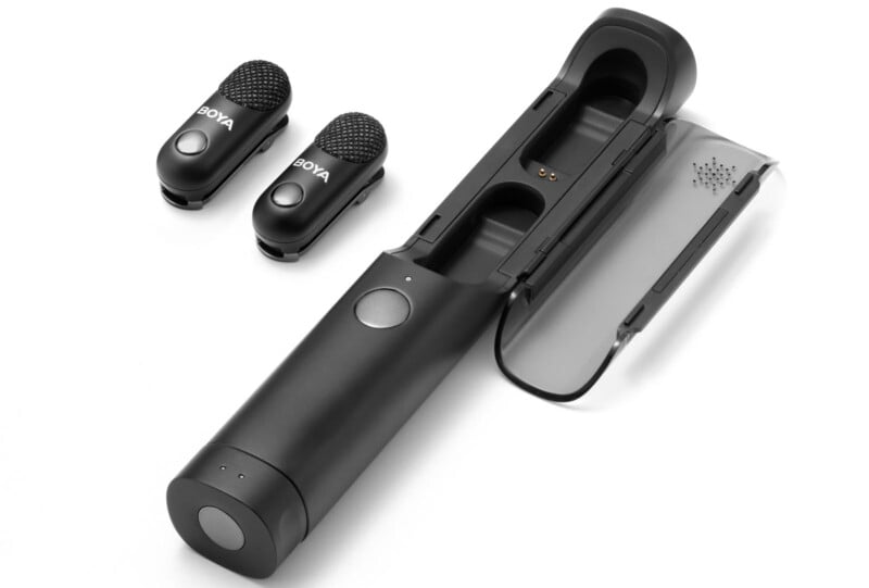 A black wireless microphone set with two small clip-on microphones and a cylindrical charging case with an open transparent lid, displayed on a white background.