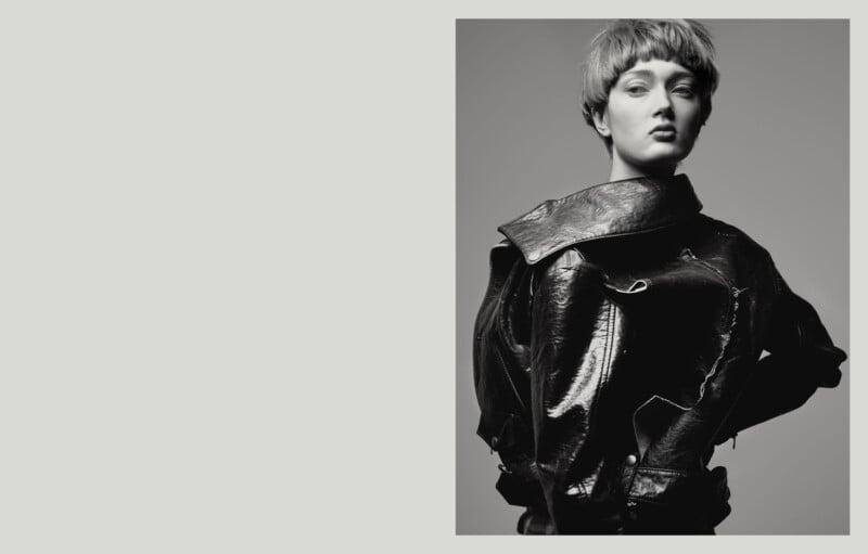 A person with short hair wearing a shiny, textured black jacket poses confidently against a plain background in a black-and-white photo.