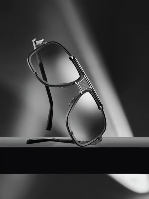 A pair of stylish black-rimmed eyeglasses is balanced on a dark surface, with dramatic lighting and shadows creating a sleek, modern, and sophisticated atmosphere.
