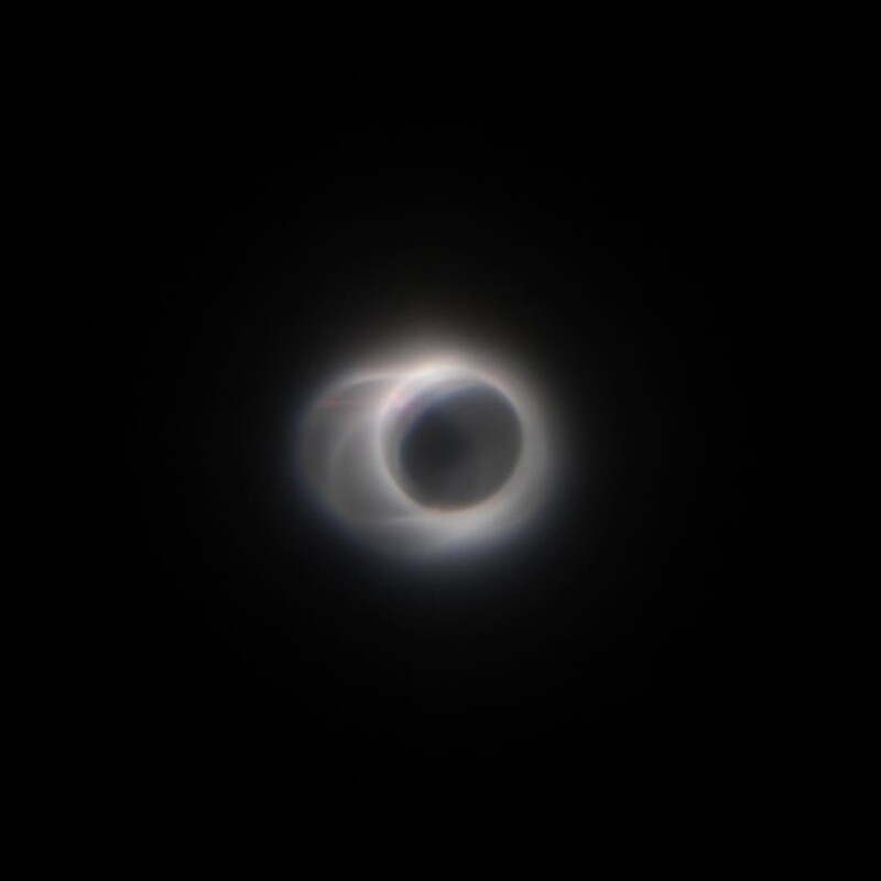 A total solar eclipse with the Moon completely covering the Sun, creating a glowing corona of light around a dark central circle against a black sky.