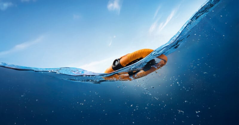A bright orange life ring floats on the surface of blue water, partially submerged, against a clear sky with wispy clouds.