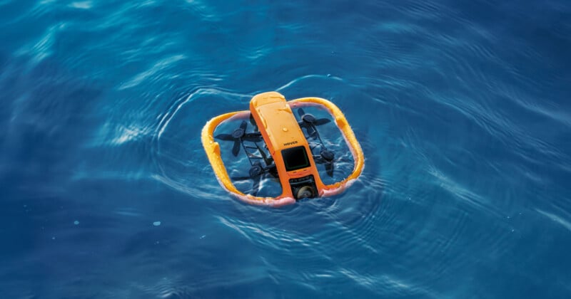 A bright orange underwater drone with yellow flotation devices floats on the surface of clear blue water.