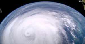 A massive hurricane with a distinct eye is seen swirling over the blue Earth, as photographed from space. White clouds spiral tightly around the storm's center, demonstrating the storm’s powerful rotation.