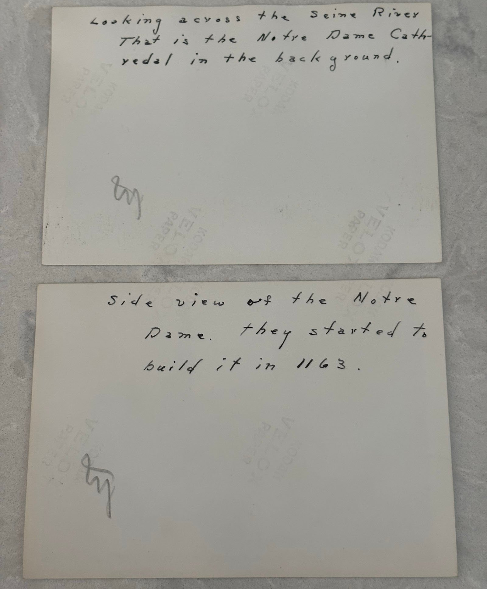 Two old photographs with handwritten notes on the back. The top note reads, "Looking across the Seine River. That is the Notre Dame Cathedral in the background." The bottom note mentions a side view of Notre Dame and its construction in 1163.